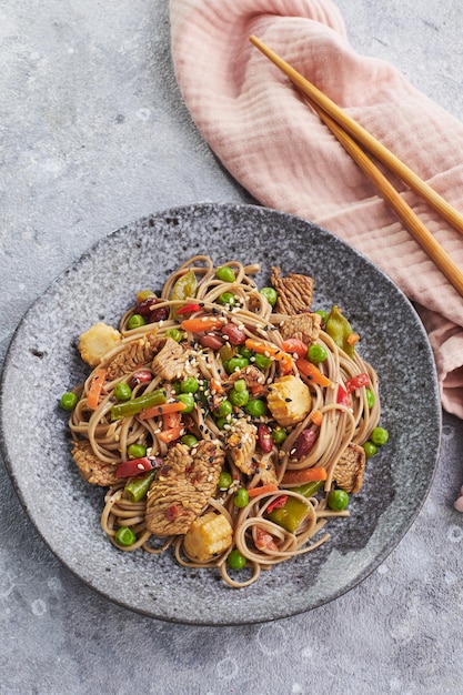 Wok com carne de peru macarrão soba milho ervilhas verdes feijão verde e cenoura servido em fundo cinza