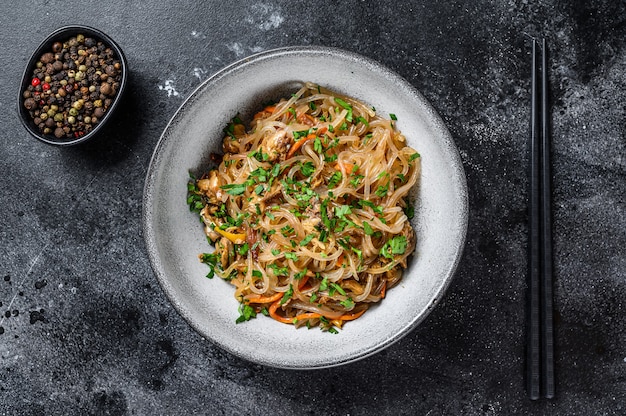 Wok macarrão quente asiático de celofane com carne de frango. mesa preta. vista do topo.