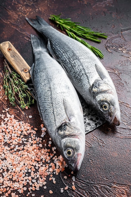 Wolfsbarsch oder Wolfsbarsch frischer roher Fisch auf einem Hackbeil mit Salz und Kräutern. dunkler Hintergrund. Ansicht von oben.