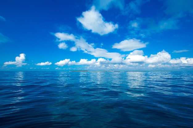 Wolken am blauen Himmel über ruhigem Meer mit Sonnenlichtreflexion