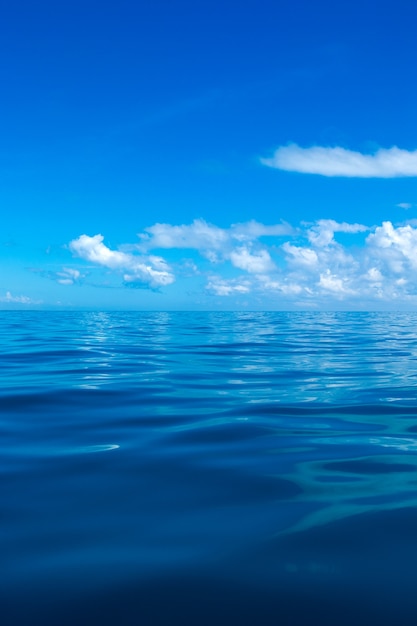 Wolken auf blauem Himmel über ruhigem Meer mit Sonnenlichtreflexion