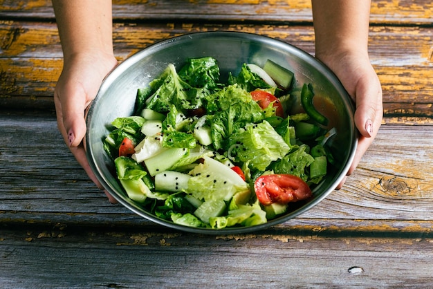 Woman39s Hände halten eine Schüssel mit Salat auf Holztisch Gesunde Ernährung