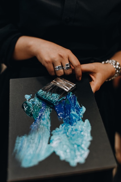 Woman39s Hand, die einen Pinsel und ein schwarzes Papier mit einer blauen abstrakten Malerei hält