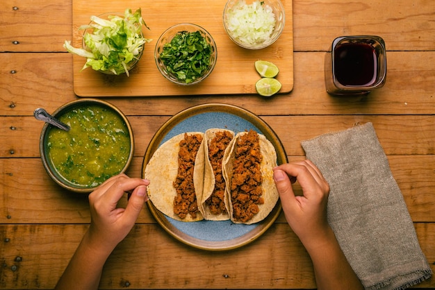 Woman39s Hand hält einen Taco aus mariniertem Fleisch Platte mit Tacos-Sauce und Gemüse auf Draufsicht des Holztischs