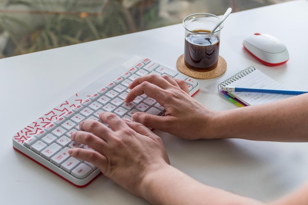 Woman39s mano escribiendo en un teclado blanco con letras rojas con café en el fondo en la mesa blanca