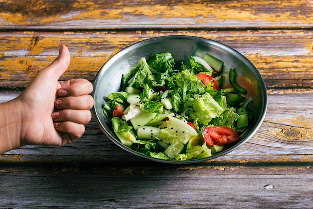 Woman39s mano gesticulando aprobación a un tazón de ensalada en una mesa de madera Comida saludable