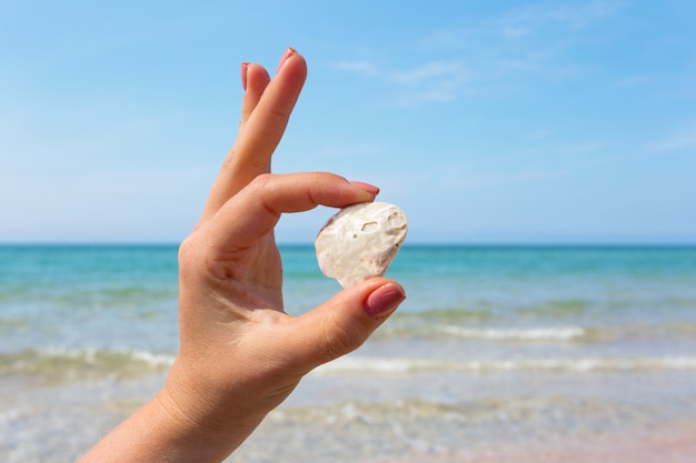 WomanaÂ mão segurando uma concha na praia.