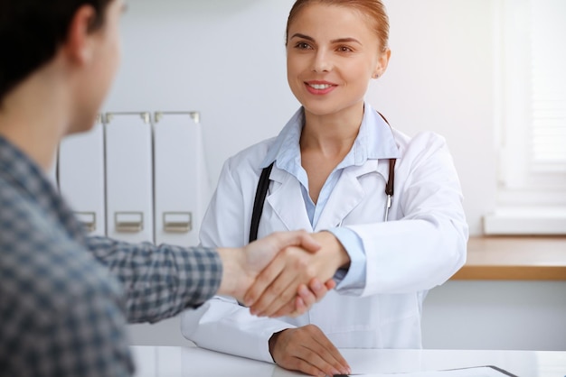 Womandoctor sonriendo mientras le da la mano a su paciente masculino Concepto de medicina