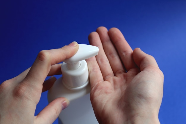 Womans dedo presiona el dispensador de una botella blanca de antiséptico sobre un fondo azul, gel antibacteriano con alcohol