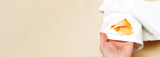 Foto womans hand halten weiße hemdkleidung mit ketchup-fleck auf einem beigen hintergrundbanner