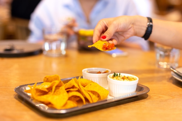 Womans Hand mit dem roten Farbnagel, der eine Tortilla-Chip-bruschetta Soße zur Mittagspause mit hat