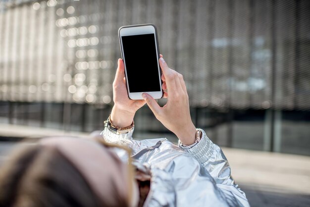 Womn usando un teléfono inteligente con pantalla vacía para copiar y pegar tumbado al aire libre en el entorno moderno