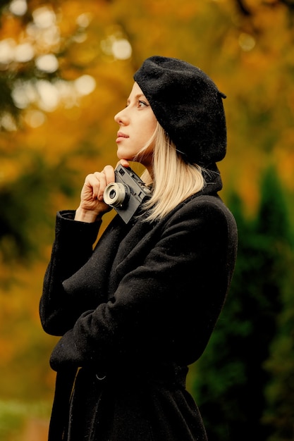 Womna im schwarzen Mantel und im Hut mit Weinlesekamera im Herbstpark