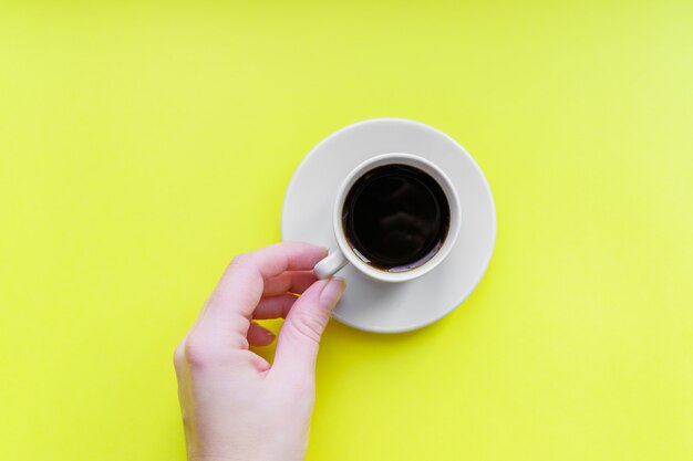 Woomans Hand, die Draufsicht des Kaffees Kaffee der minimalen Ebene hält, lag auf gelbem Hintergrund.