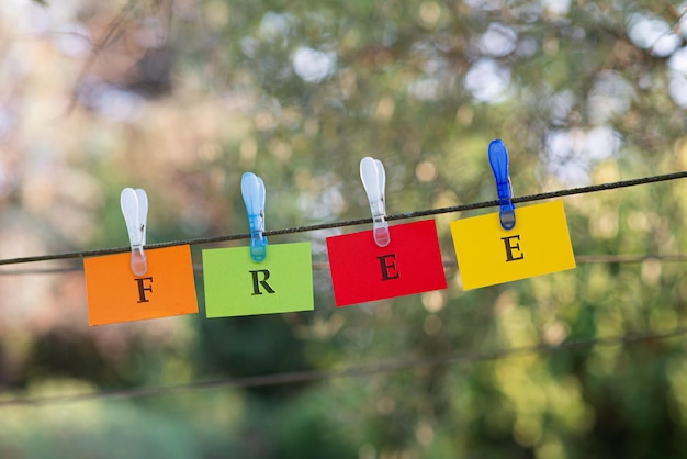 Foto word free buchstabiert auf bunten papieren, die an einem seil hängen, das mit wäscheklammern draußen in grüner natur befestigt ist.