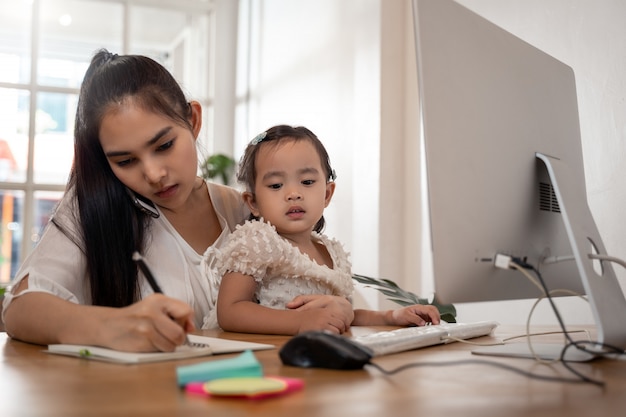 Work from Home-Konzept. Mutter und Tochter nutzen einen Computer und das Internet, während die Mutter von zu Hause aus arbeitet