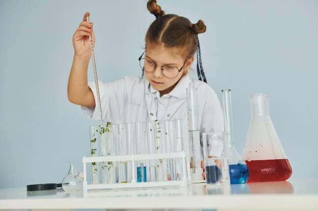 Workes con líquido que está en tubos de ensayo Niña en abrigo jugando a un científico en el laboratorio mediante el uso de equipos