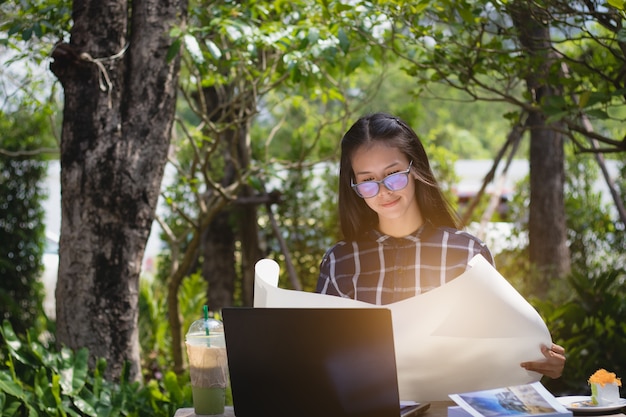 workingwoman, estudante que olha o trabalho de papel com relaxa no jardim no feriado.