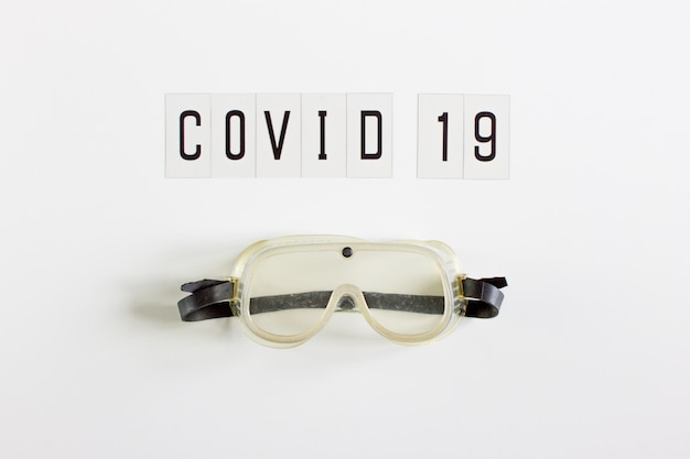 Wort "Covid 19" in Schwarz auf weißem Hintergrund mit Platz zum Schreiben. Mit Schutzbrille für medizinisches Personal.