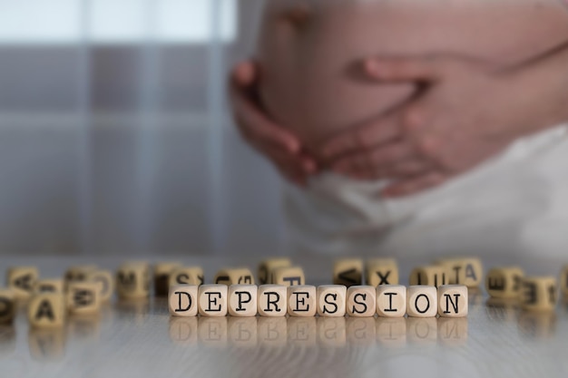 Wort DEPRESSION bestehend aus Holzbuchstaben. Schwangere Frau im Hintergrund