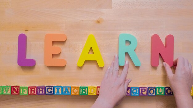 Wort lernen aus mehrfarbigen Holzbuchstaben auf Holztisch.