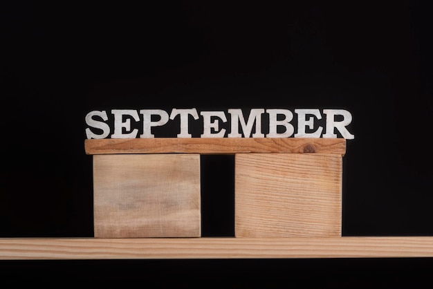 Wort September aus Holzbuchstaben auf schwarzem Hintergrund Vorderansicht Herbstkalender Herbstmonat