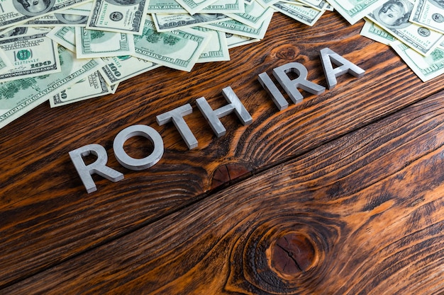 Worte ROTH IRA auf Holzoberfläche durch Metallbuchstaben mit US-Dollar-Banknoten gelegt