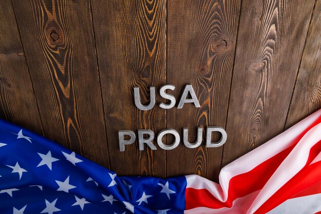 Foto worte usa stolz mit silbernen metallbuchstaben auf braune holzoberfläche mit flagge der vereinigten staaten von amerika gelegt