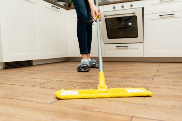 Foto worth housewife cleaning floor em casa. mulher adorável lava pisos de madeira de um laminado em uma cozinha brilhante