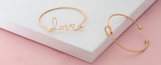 Wortliebe und Knotenform goldene Armbänder auf rosa und weißem Hintergrund mit Kopienraum