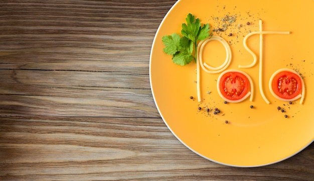 Wortnudeln aus gekochten Spaghetti auf dem Teller mit Tomaten, Kräutern und Gewürzen auf Holztisch-Draufsicht.
