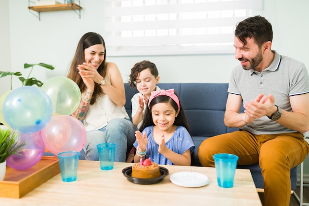Wow! Aufgeregte Eltern schmeißen eine Geburtstagsfeier für ihre süße Tochter. Lateinische Familie klatscht und feiert zu Hause den Geburtstag eines Kindes