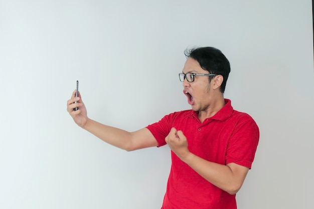 Wow, la cara de un joven asiático se sorprendió por lo que vio en el teléfono inteligente con un fondo gris aislado