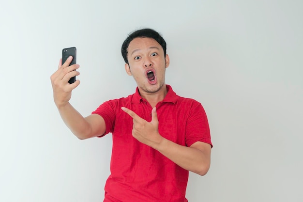 Wow, la cara de un joven asiático se sorprendió por lo que vio en el teléfono inteligente con un fondo gris aislado