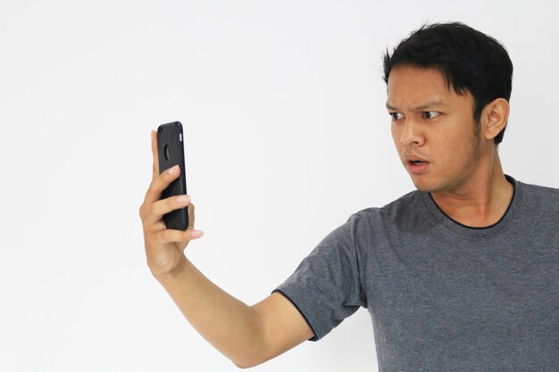 Wow, la cara de tu hombre asiático sorprendió lo que vio en el teléfono inteligente con un fondo gris aislado
