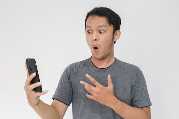 Wow, la cara de tu hombre asiático sorprendió lo que vio en el teléfono inteligente con un fondo gris aislado