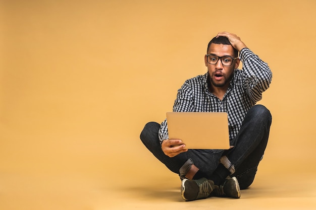 Wow Concepto de trabajo en línea Hombre de negocios afroamericano relajado trabajando y navegando por Internet en una computadora portátil Freelancer sentado en el piso y escribiendo aislado sobre beige