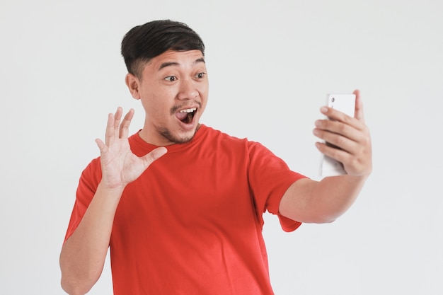 Wow la expresión de la cara del hombre asiático en camiseta roja se sorprende mientras saluda en el teléfono inteligente