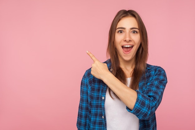 Wow, schau dir verrückte Werbung an Porträt eines erstaunten brünetten Mädchens in kariertem Hemd, das auf einen leeren Platz für Werbeinhalte zeigt und eine Überraschung ausdrückt Studioaufnahme isoliert auf rosa Hintergrund