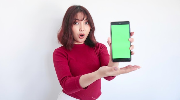 Wow und Shock Asiatisches schönes Mädchen zeigt auf Greenscreen-Telefon mit verschwommenem Hintergrund im Gesicht in Weiß