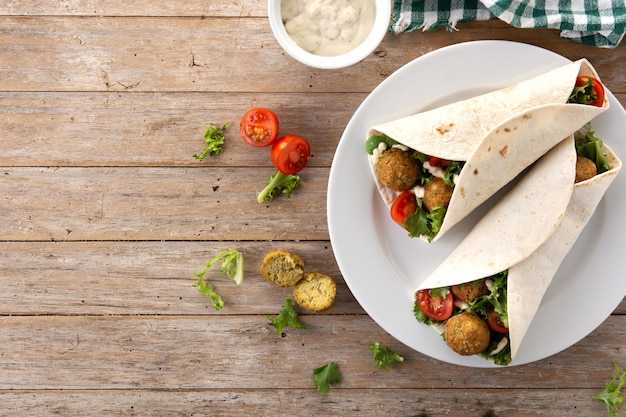 Wrap de tortilha com falafel e legumes na mesa de madeira