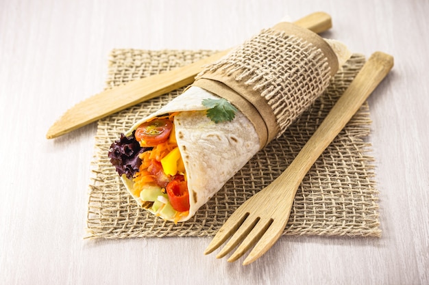 Wrap de tortilha vegana, rolo vegetariano com vegetais grelhados, pimenta, lentilha, tomate e repolho, em uma superfície de madeira rústica