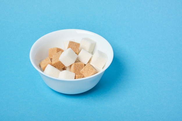 Würfel aus braunem und weißem Zucker in einer weißen Schüssel auf einer blauen Oberfläche kopieren Raum