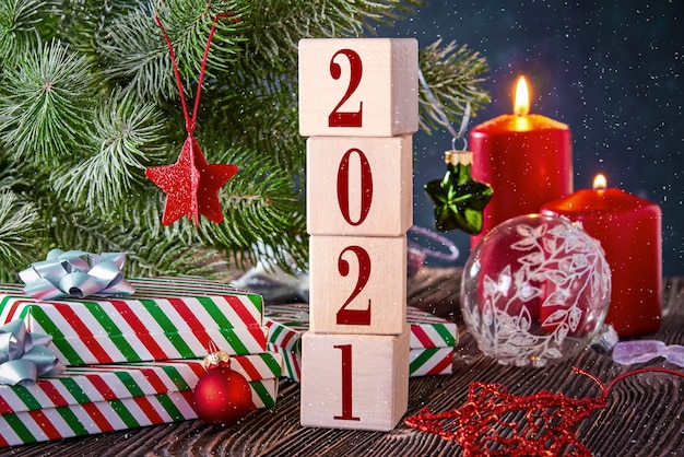Würfel mit den Nummern 2021 auf einem Weihnachtshintergrund mit Geschenken in Kisten, verziert mit einem Fichtenzweig und brennenden Kerzen. Neujahrshintergrund mit freiem Platz für Text.