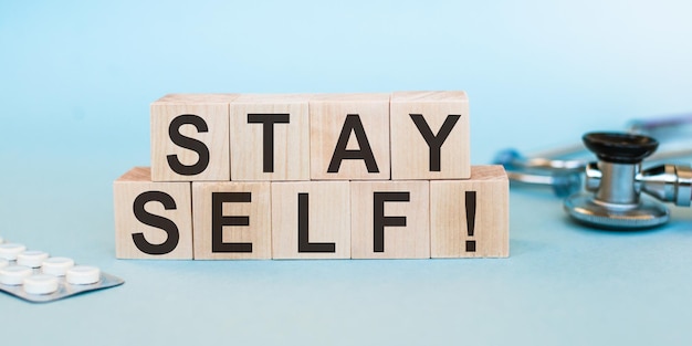 Würfel mit Text STAY SELF auf blauem Hintergrund mit Tablets und Stethoskop