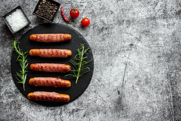 Würstchen auf einem schwarzen Teller mit einer Schüssel Gewürzen und Tomaten.