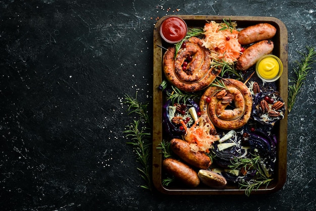 Würstchen gebacken Kohl Sauerkraut Gewürze und Gemüse Ansicht von oben auf einem schwarzen Stein Hintergrund