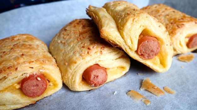 Würstchen im Teig auf einem Backblech mit Backpapier Leckere frische Torten aus dem Ofen Hefeteig kulinarische Produkte mit Milchwürsten Bestreuung mit Sesam