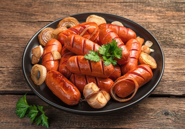 Würstchen mit gebratenen Zwiebeln, Knoblauch und frischer Petersilie auf einem hölzernen Hintergrund. Nahaufnahme.