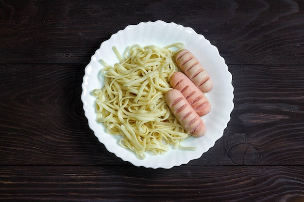 Würstchen und Spaghetti in weißer Platte auf dunklem Holzhintergrund